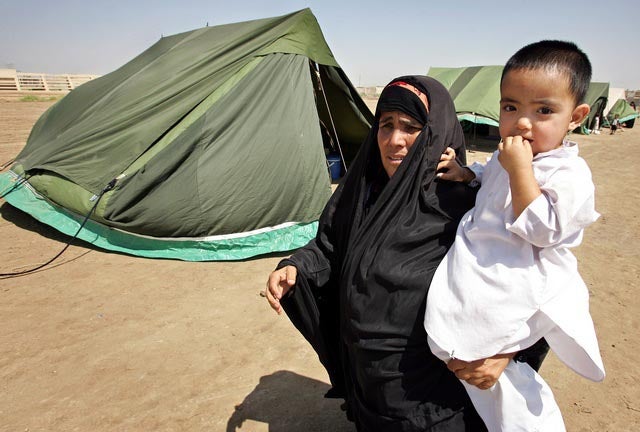 An Iraqi woman carries a child between tents in a refugee camp in Baghdad. July 2006. &copy; 2006 REUTERS 