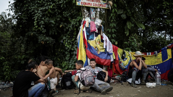 Migrants sit under a sign marking the Panama-Colombia border