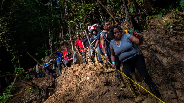 Migrants and asylum seekers climb down a muddy hillside trail in the jungle