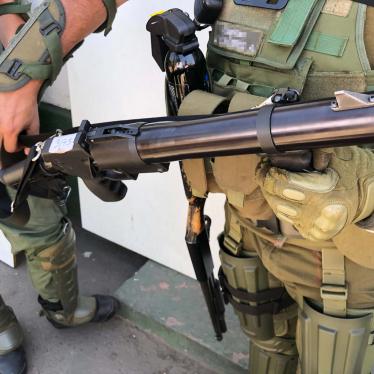 A police captain holds a teargas gun. A pellet shotgun hangs on his right side. 