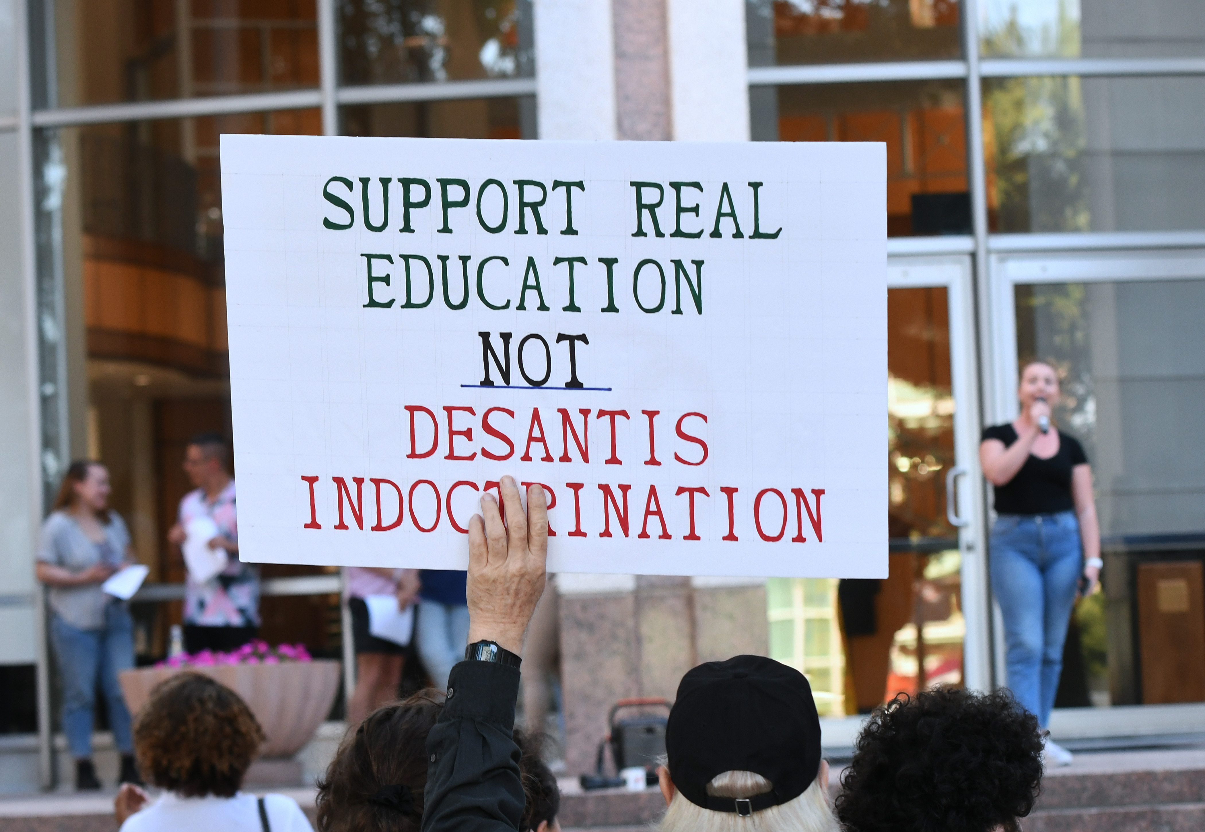 A man holds up a sign that reads "support real education not desantis indoctrination"