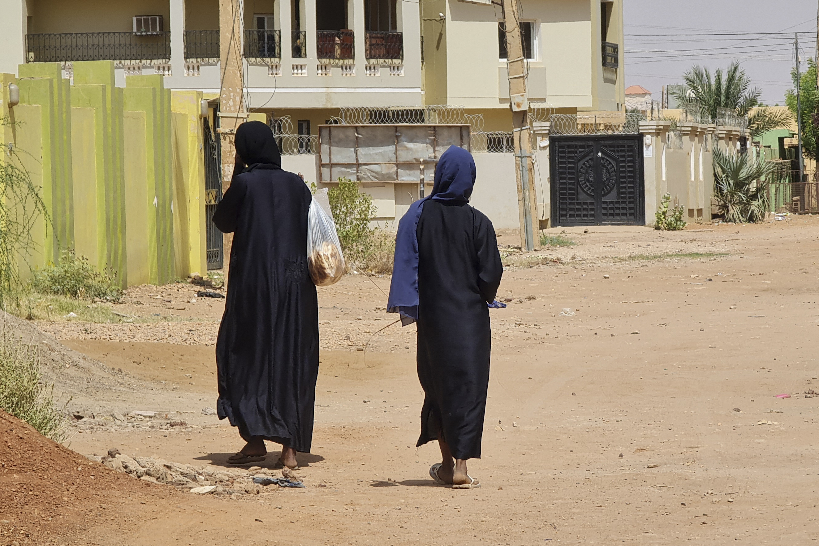 امرأتان تسيران في شارع خالٍ من المارة في حي جبرة في الخرطوم، في 28 مايو/أيار 2023، بينما يستمر القتال بين الجنرالين المتناحرين. 
