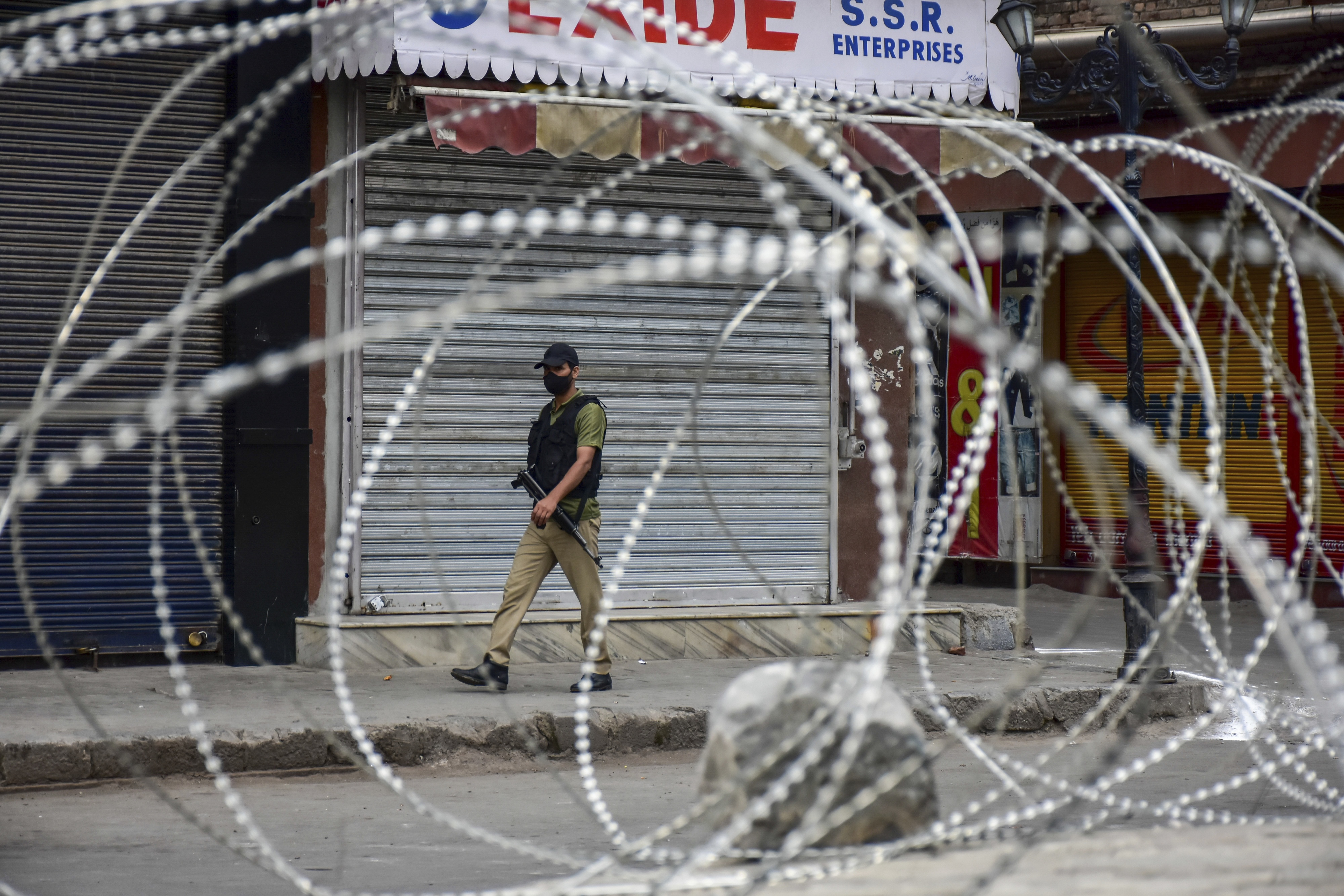Un membre d’une force paramilitaire indienne patrouillait dans une rue dont l’accès était partiellement bloqué par une clôture en fil de fer barbelé à Srinagar, au Jammu-et-Cachemire, le 15 août 2021, Jour de l'indépendance de l'Inde.