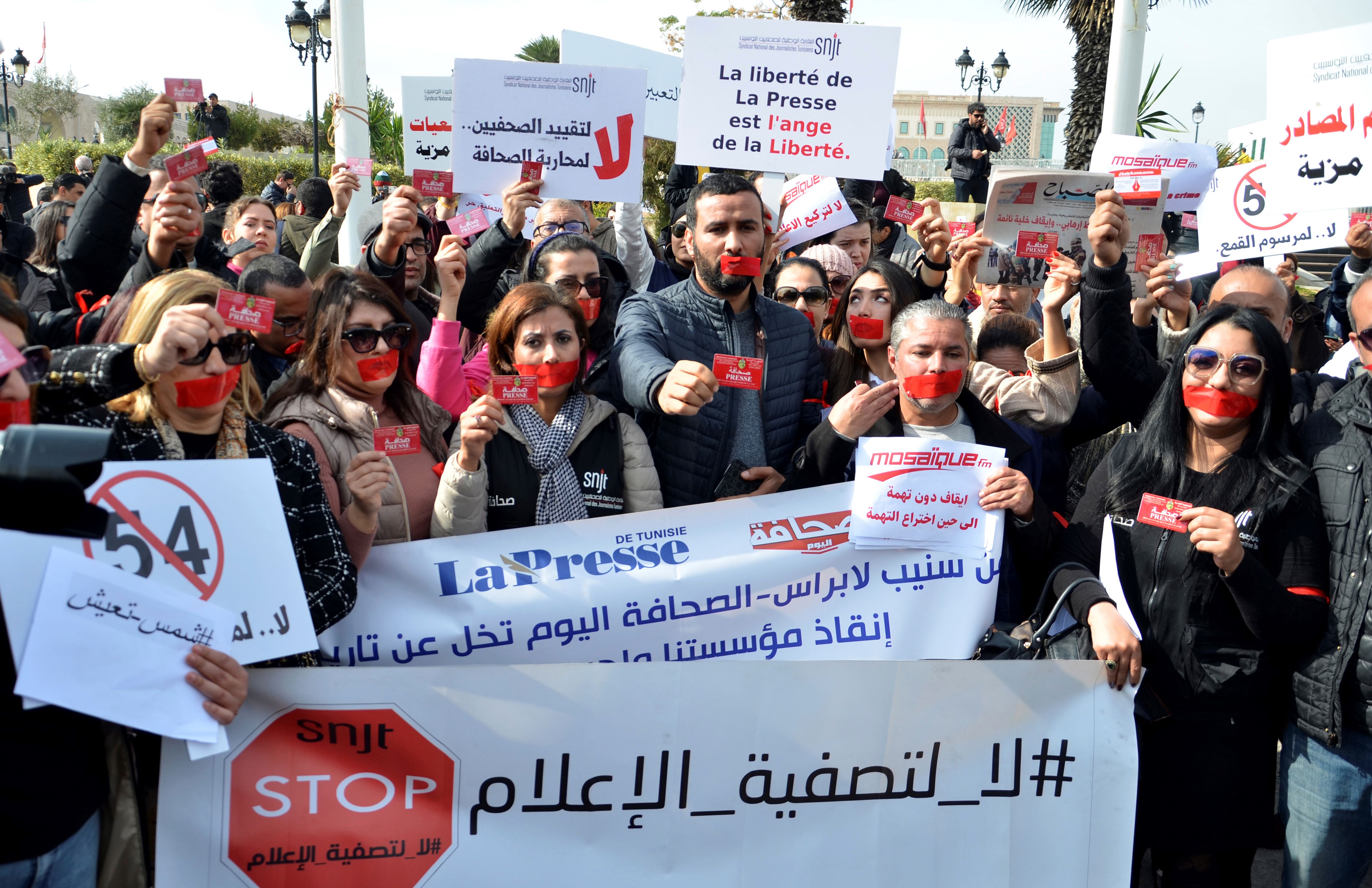 Protesters with red tape over their mouths hold placards