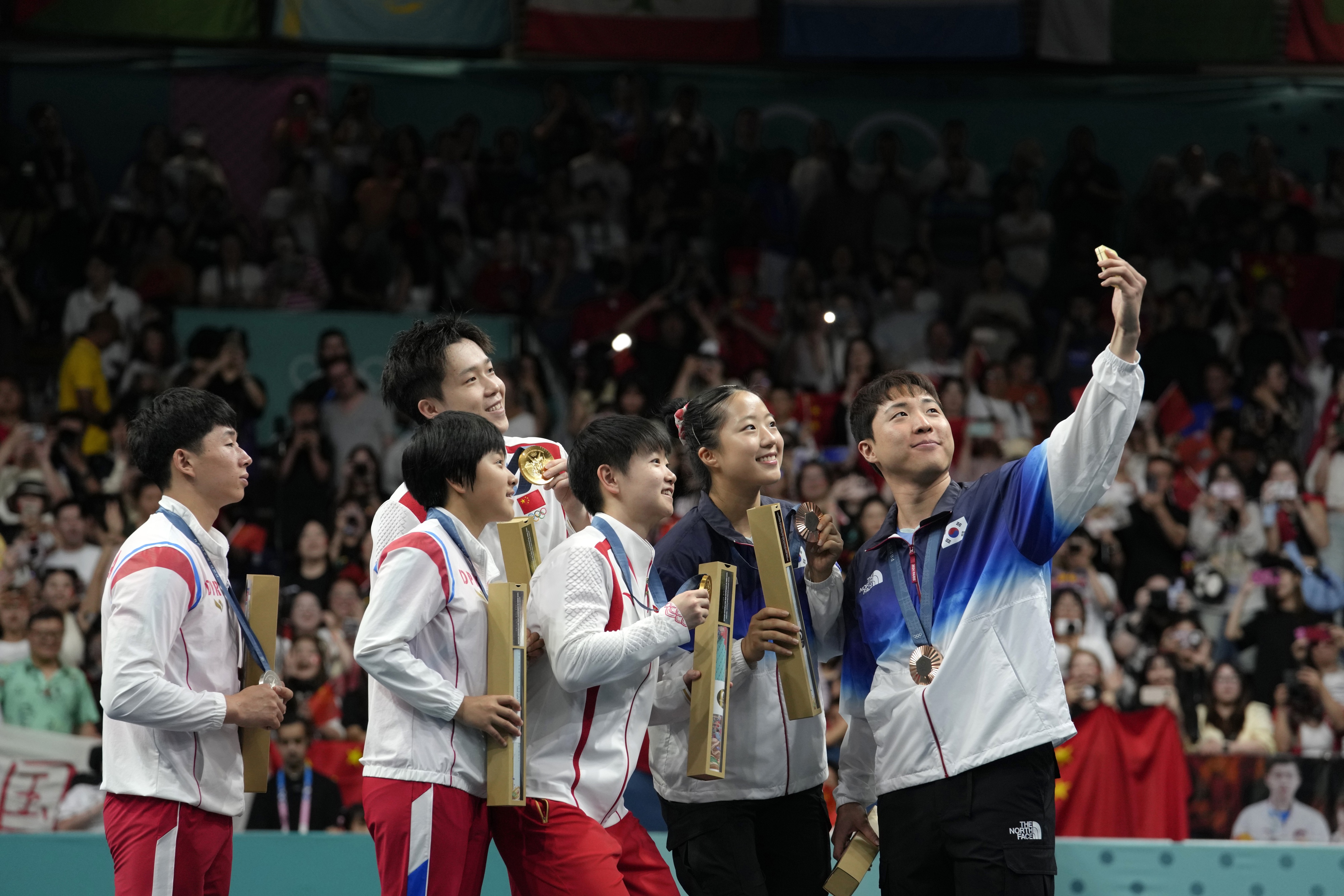 Le joueur de tennis de table sud-coréen Lim Jong-hoon, à droite, qui avec sa coéquipière Shin Yu-bin a remporté la médaille de bronze en double mixte aux JO de Paris, prenait un selfie peu après la cérémonie de remise des médailles, le 30 juillet 2024, avec d’autres joueurs : la paire nord-coréenne Ri Jong Sik et Kim Kum (médaille d’argent), à gauche, ainsi que la paire chinoise Wang Chuqin et Sun Yingsha (médaille d’or), au centre.