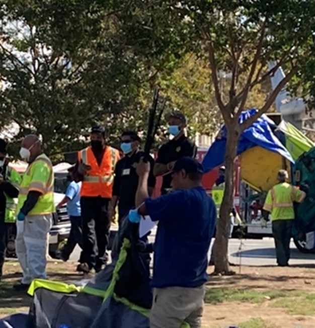 A man packs up his tent while city officials look on