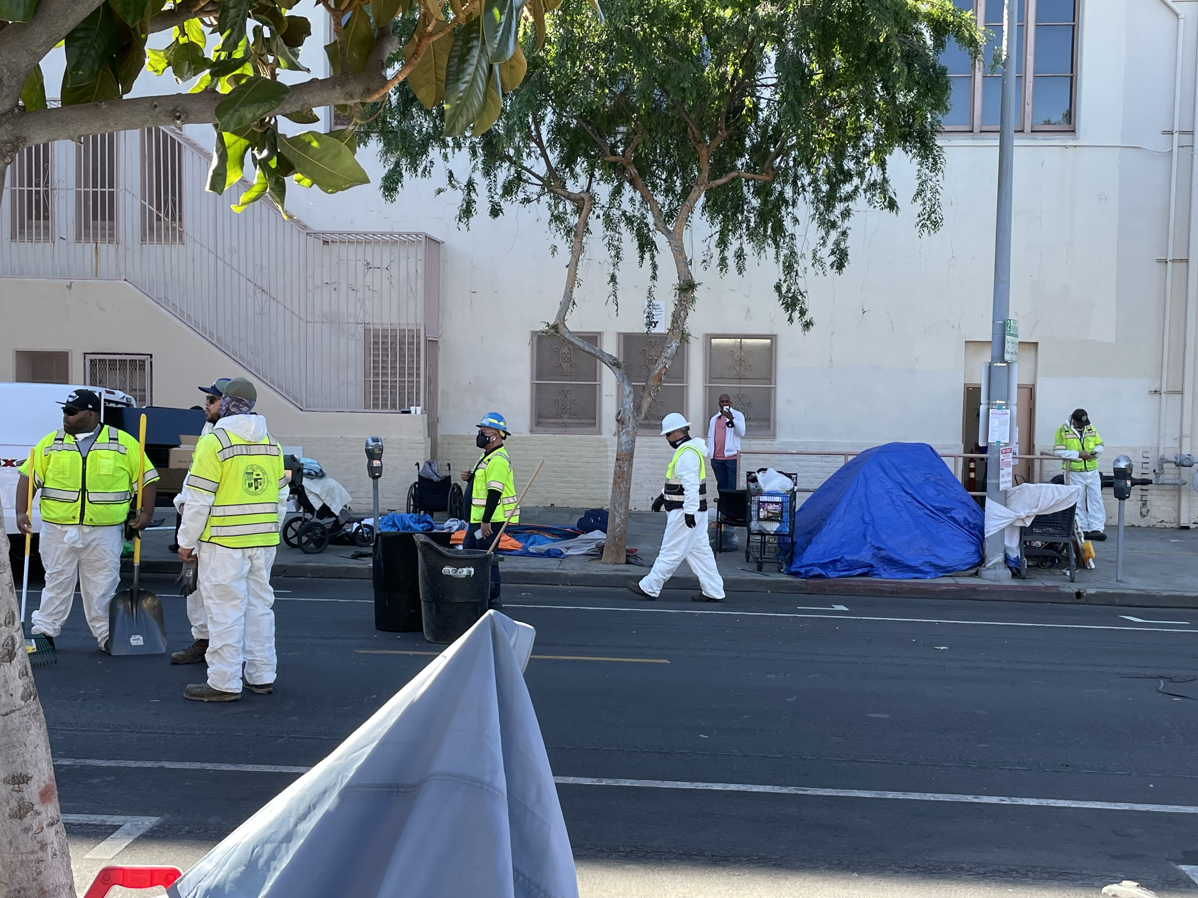 Workers conduct a sweep of a tent encampment