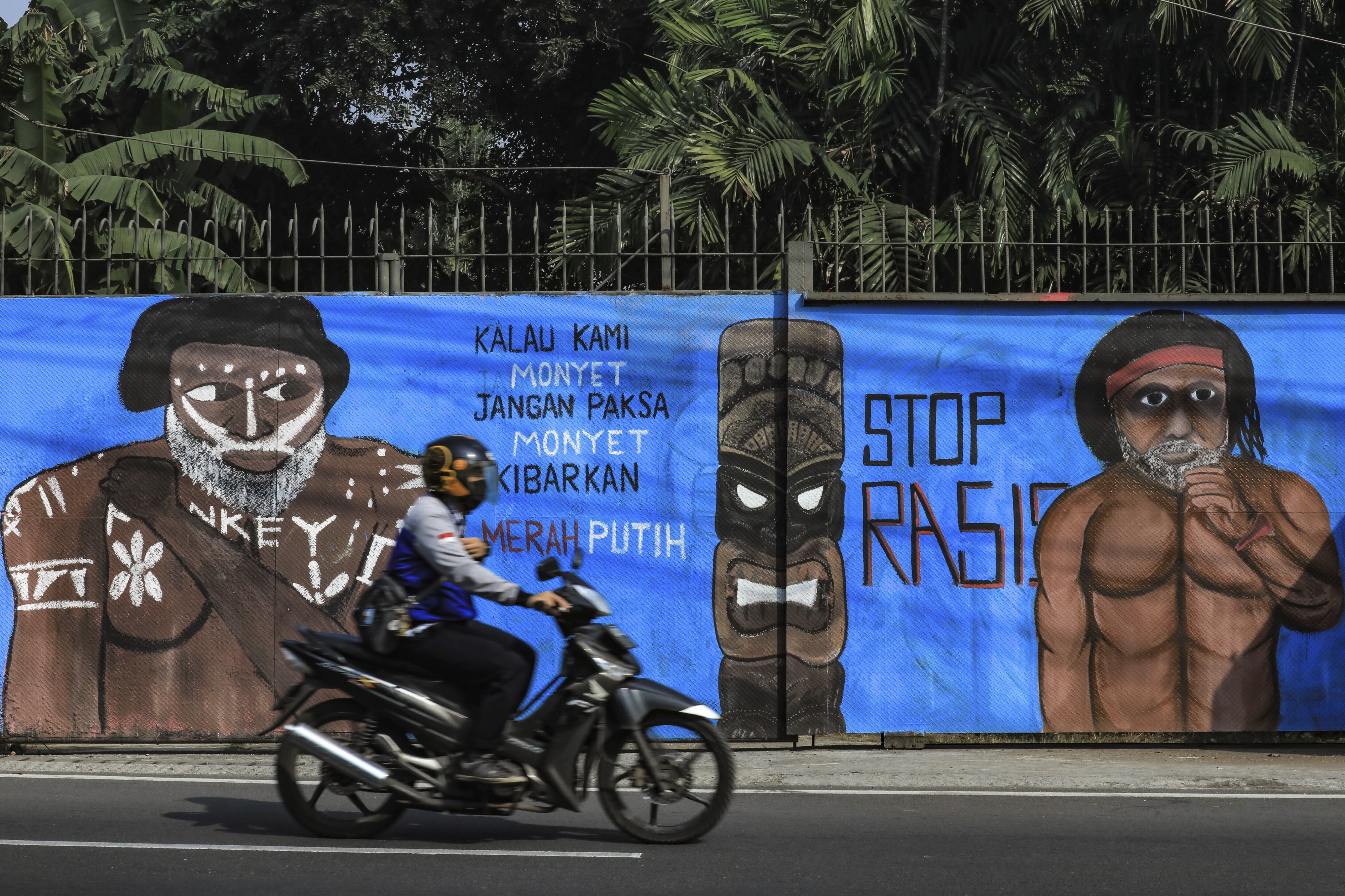 A motorcycle drives past two murals on the side of a building