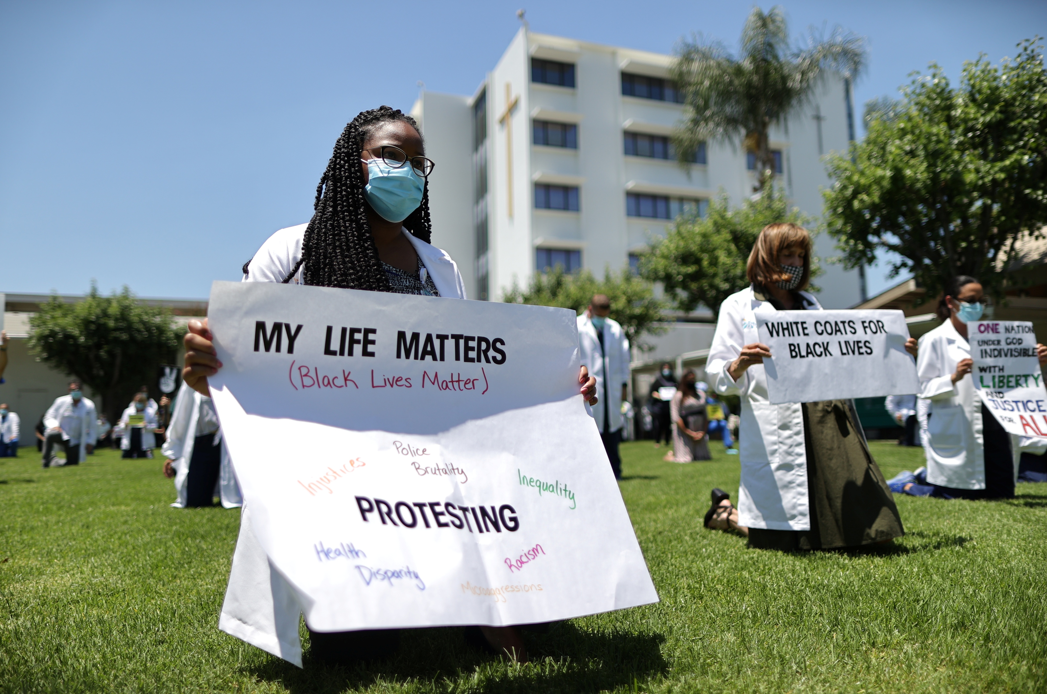 A doctor kneels while holding a sign during a "White Coats for Black Lives" tribute for George Floyd and other African-Americans who died in police custody, outside of a hospital in West Covina, near Los Angeles, California, US, June 11, 2020.