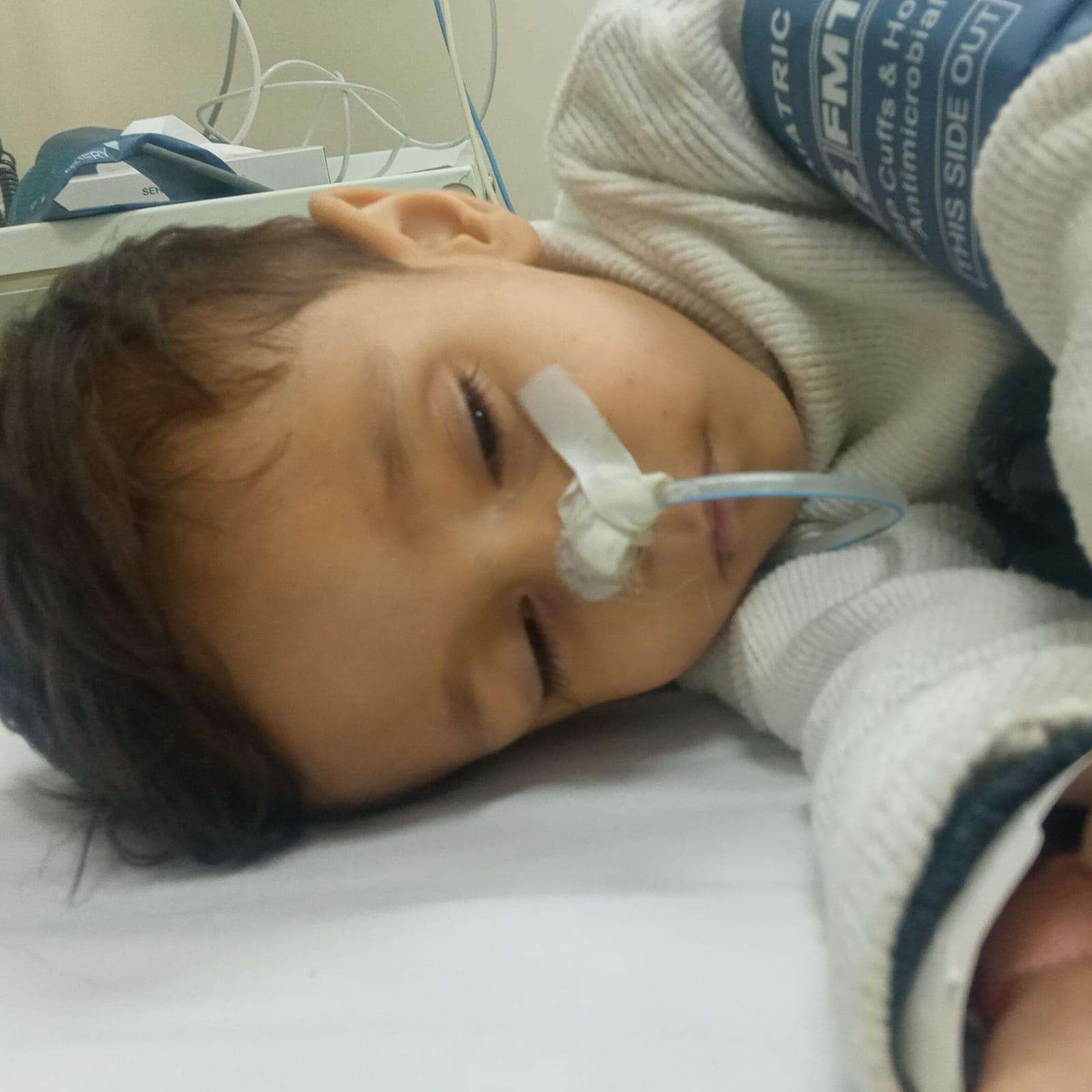 A boy lying down in a hopistal bed with a feeding tube