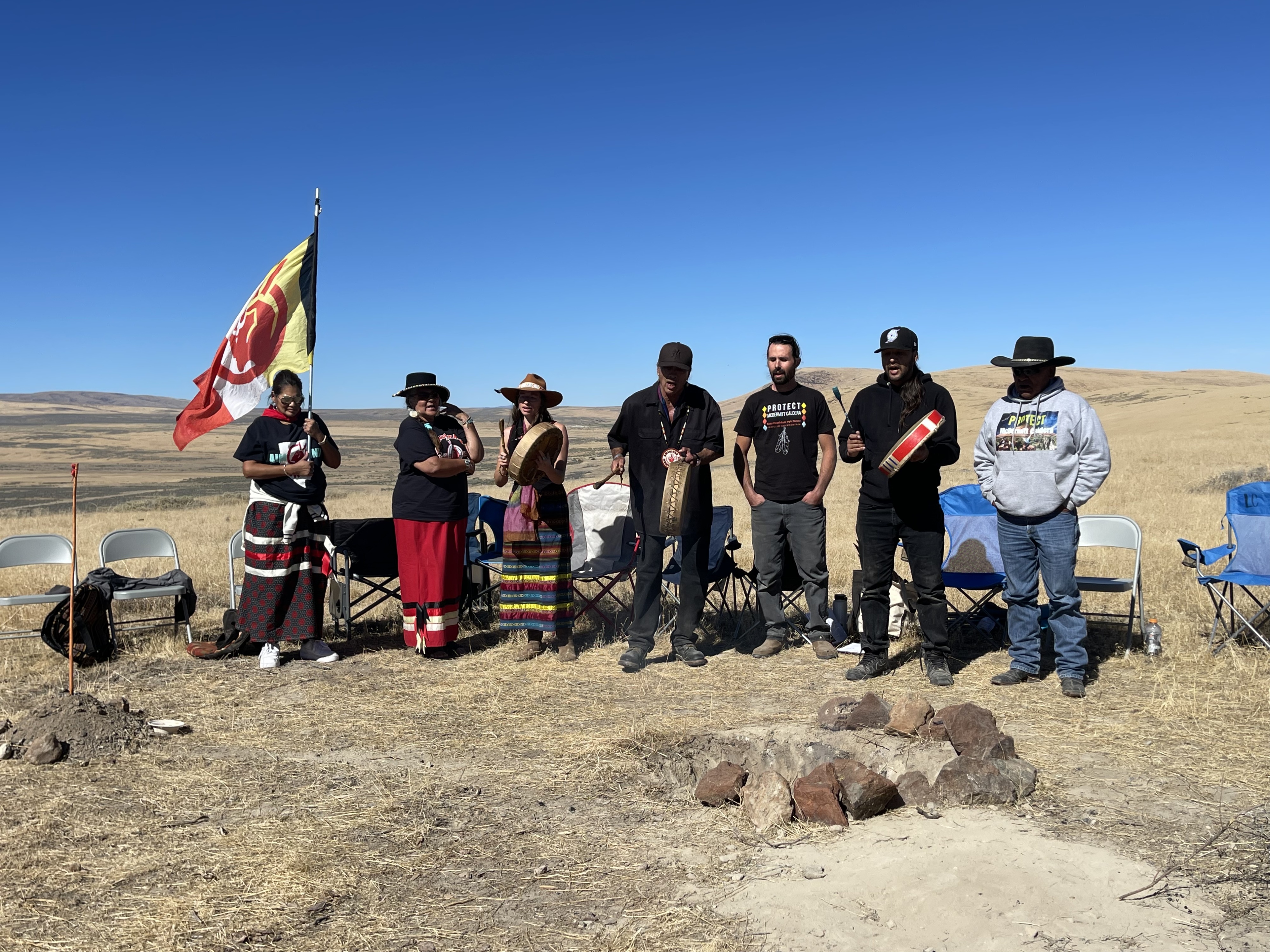 Members of People of Red Mountain and their supporters stand around a fire