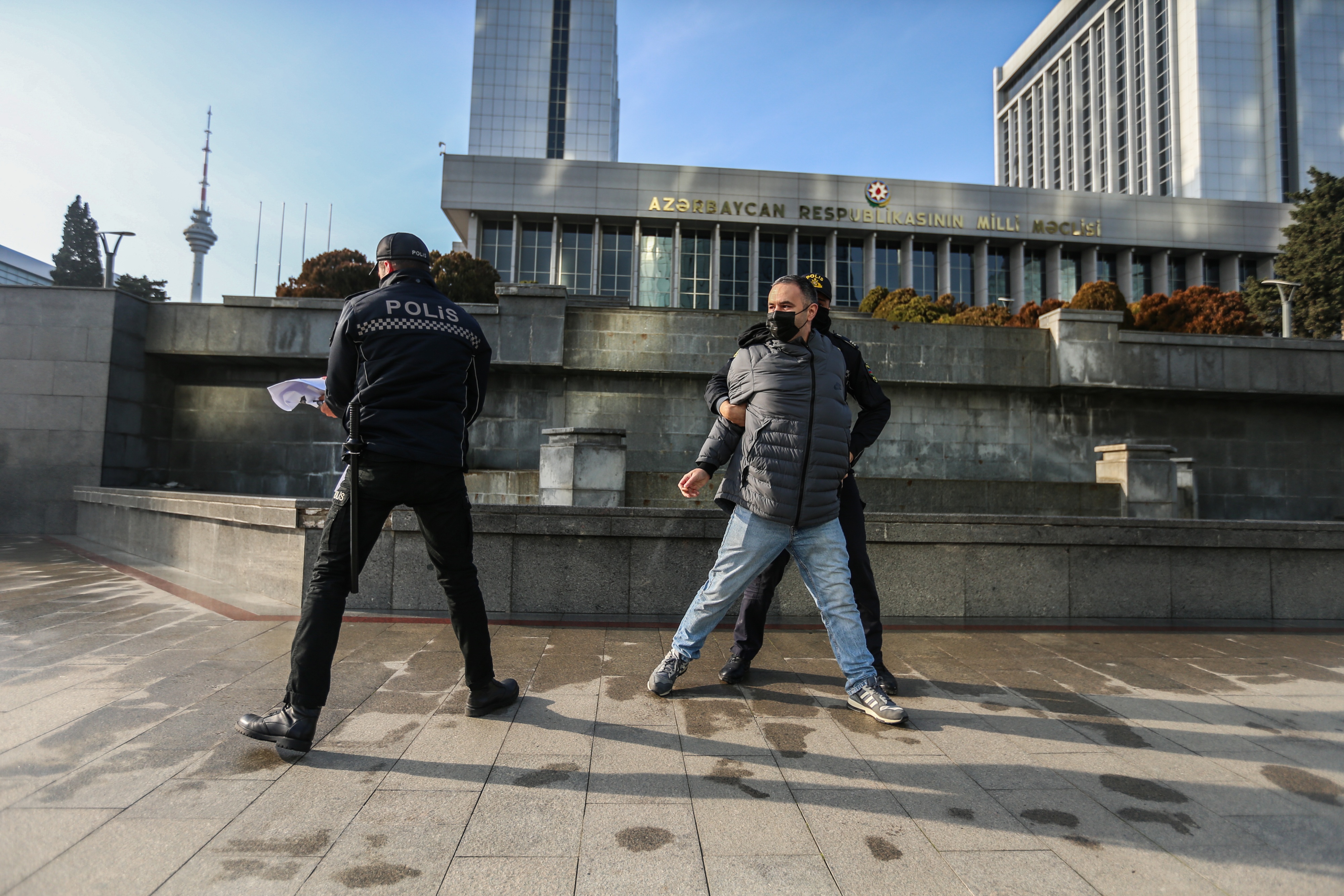 La polizia sequestra un manifesto con la scritta "Il giornalismo non è un crimine" durante una protesta di giornalisti di fronte al palazzo del parlamento dell'Azerbaigian, il 28 dicembre 2021, a Baku. Nel novembre 2023, le autorità azere hanno arrestato il direttore di Abzas Media, Ulvi Hasanli, a destra nella foto, e cinque dei suoi colleghi con accuse false. Tutti e sei sono ancora in custodia cautelare.