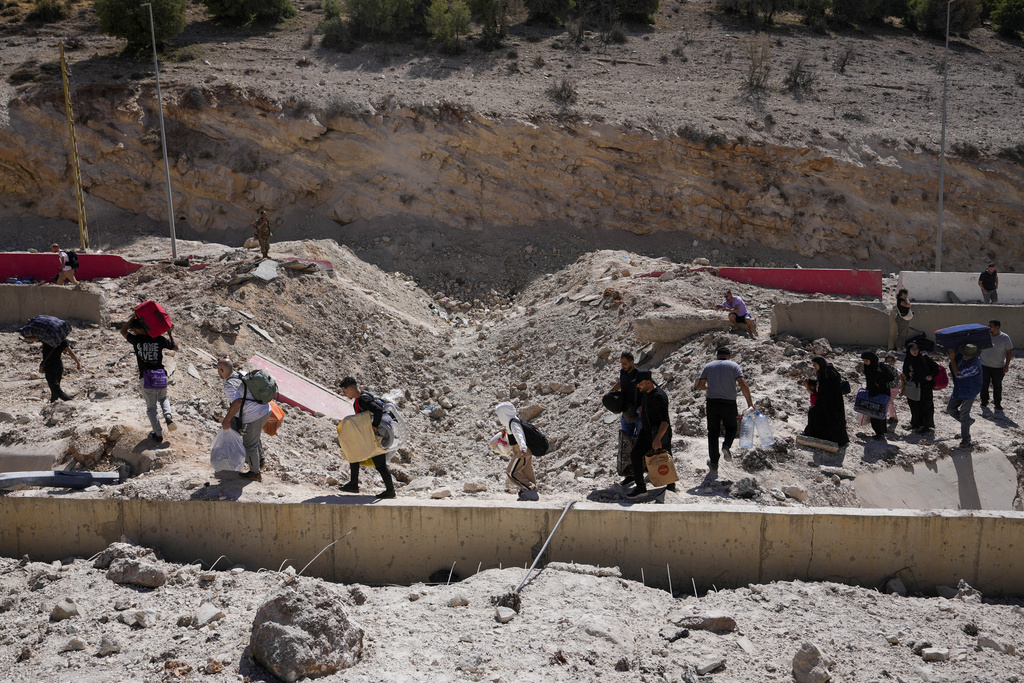 People carry their luggage as they cross into Syria on foot, through a crater caused by Israeli airstrikes aiming to block Beirut-Damascus highway at the Masnaa crossing, in the eastern Bekaa Valley, Lebanon, October 5, 2024.