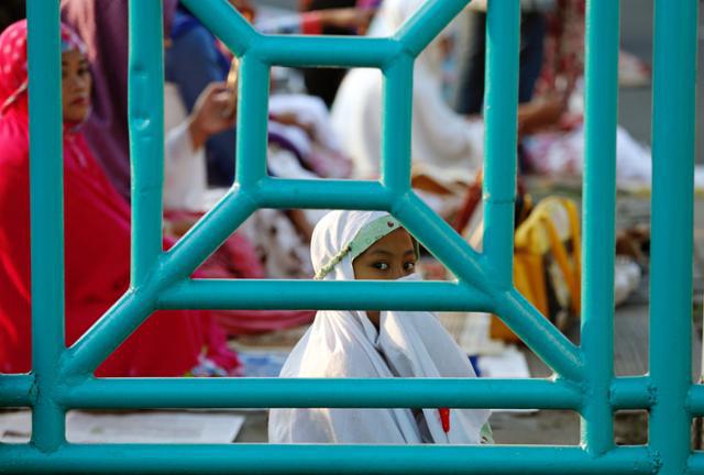 A girl is seen through a fence before prayers for the Muslim holiday of Eid Al-Adha on a street in Jakarta, Indonesia September 12, 2016.