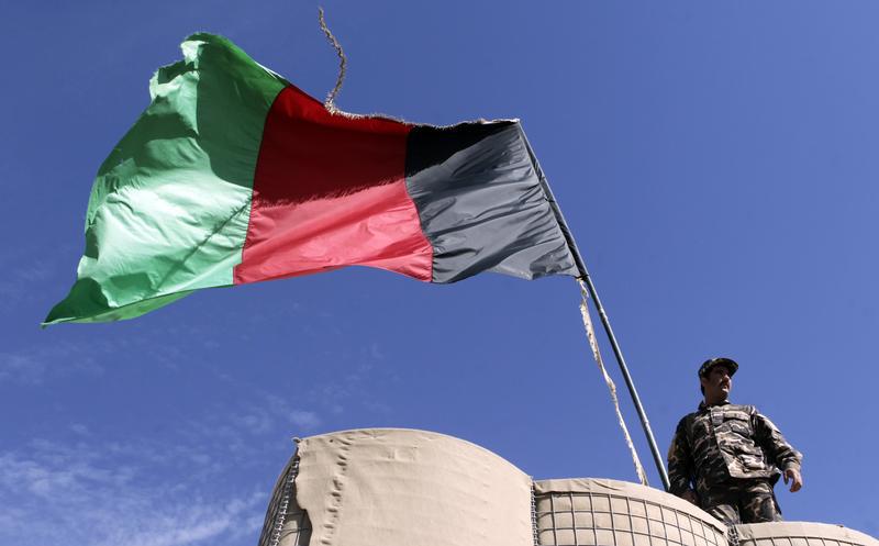 An Afghan National Directorate of Security (NDS) police stands guard next to an Afghanistan flag at a guard post of a police camp in Now Zad district in Helmand province, southwestern Afghanistan November 6, 2012.