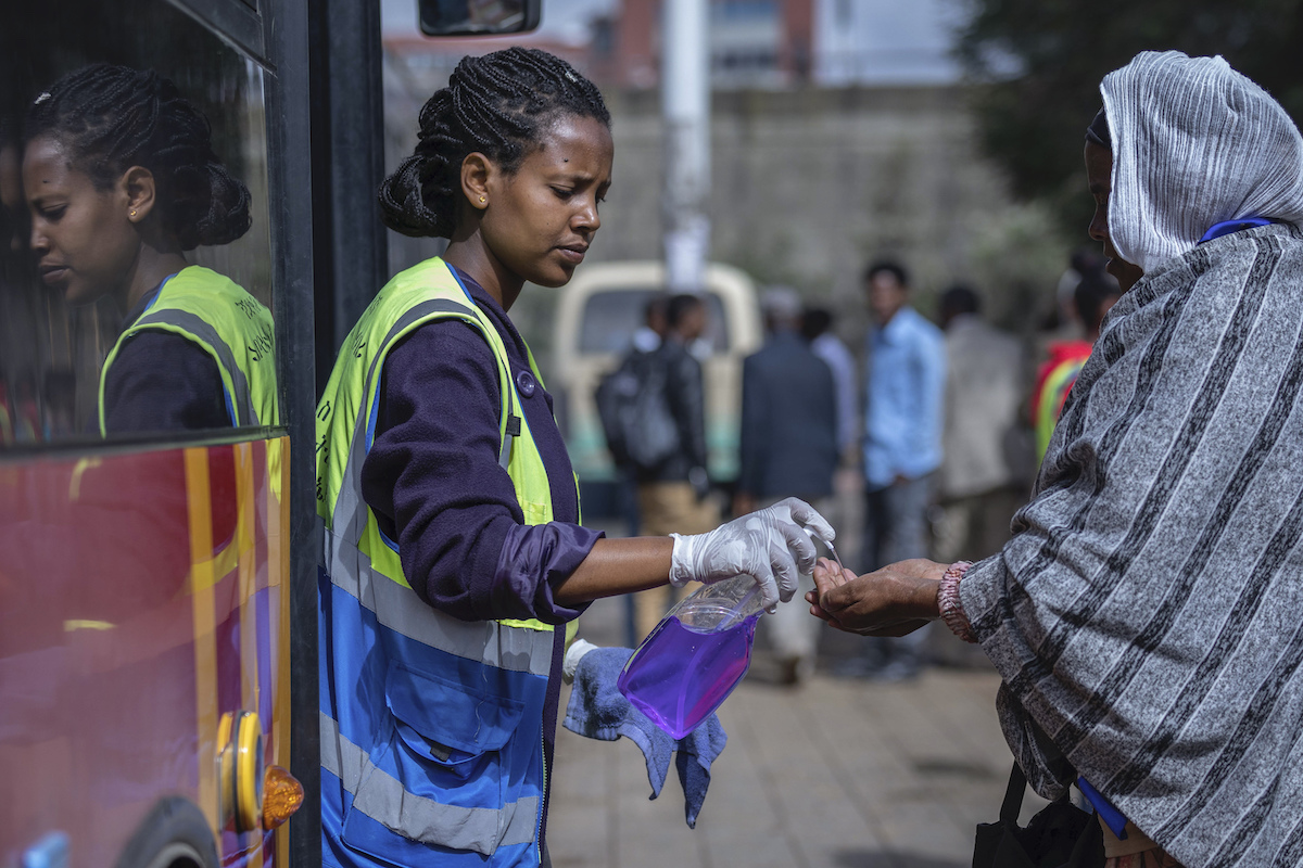 A volunteer provides hand sanitizer to passengers entering a bus