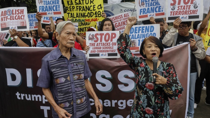 A man and a woman hold microphones in front of a crowd holding protest banners