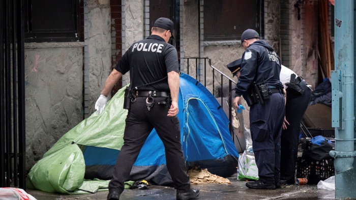 Police look into a tent at an encampment for unhoused people