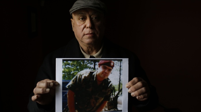 A man holds a photo of his son wearing a military uniform