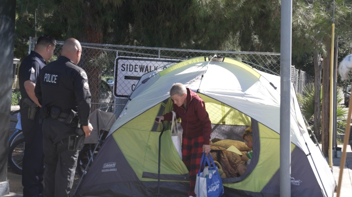 Police remove an unhoused woman from her tent