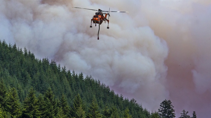 A helicopter flies over a wildfire in a forest