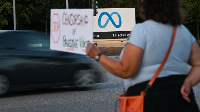 A person holding a protest sign outside of the Meta headquarters