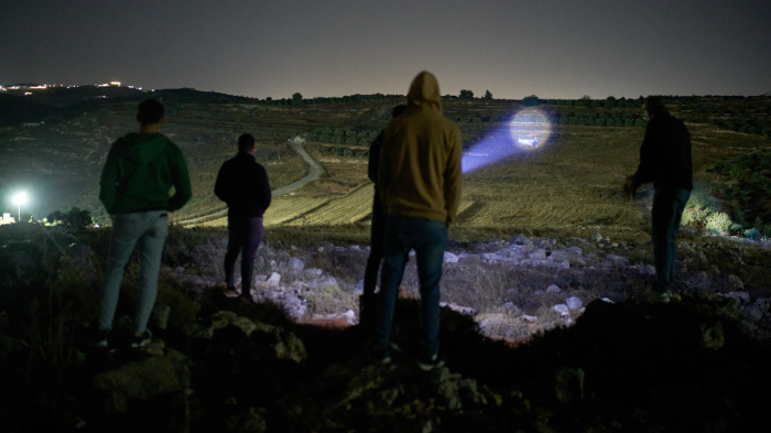 A Palestinian uses a flashlight on a nearby hill while taking part in a night watch with other volunteers to deter settler attacks on the West Bank village of Sinjil, July 16, 2026.