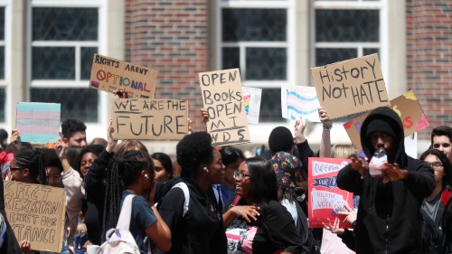 A group of high school students hold signs in front of a school building