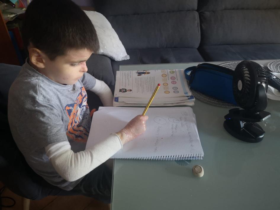 Leo Osorio, 9, der eine körperliche Behinderung hat, macht in seinem Wohnzimmer im andalusischen Sevilla (Spanien) seine Hausaufgaben und benutzt einen kleinen Ventilator, um sich abzukühlen.