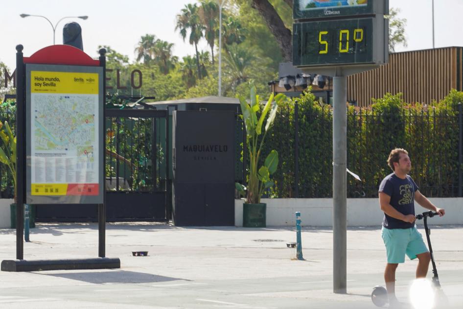 A sign in Paseo de las Delicias, Seville (Andalusia, Spain) on July 25, 2022, displaying the high temperature of 50 degrees Celsius, and a man using his scooter.