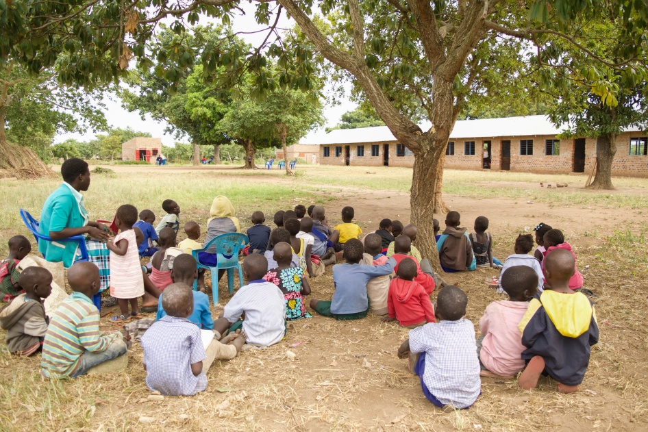 A teacher conducts a class outside with a group of small children
