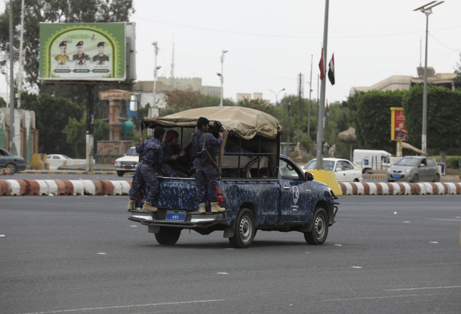 Soldiers in uniform ride in a military vehicle down a city street