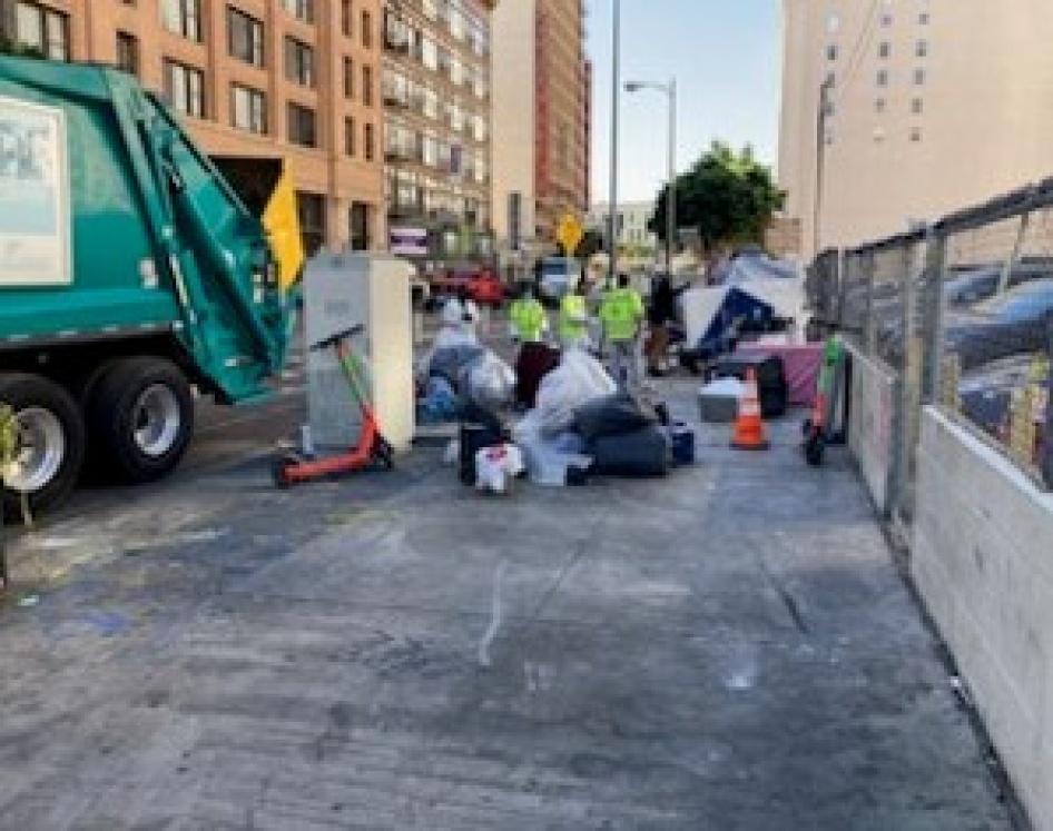 LASAN workers loading items from the unhoused encampment into the trash compactor truck