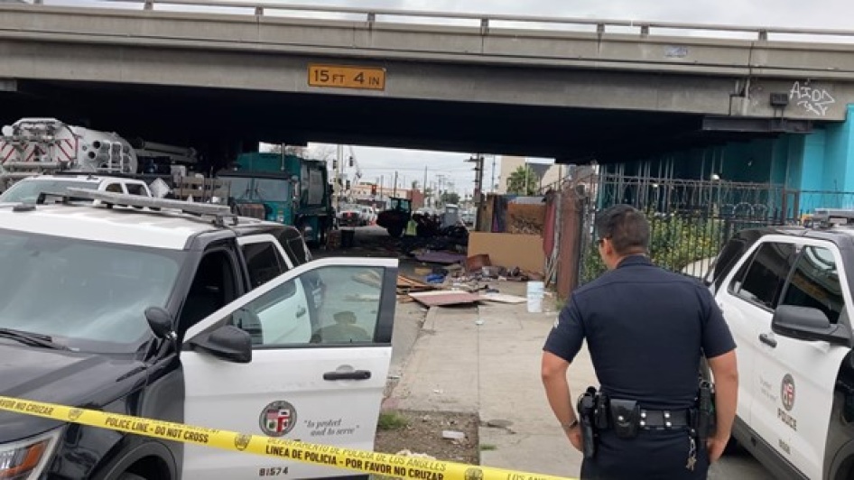 Police next to a tent encampment underneath a highway overpass