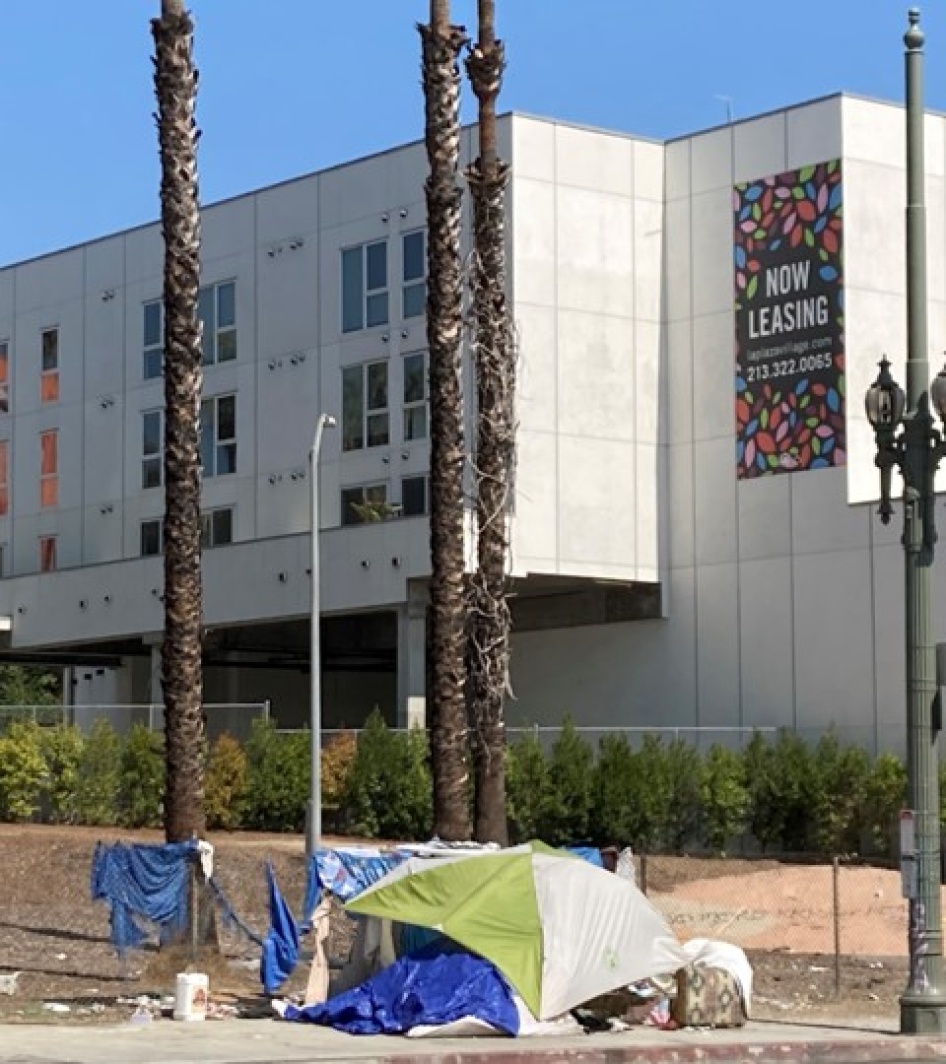 Tent encampment in front an apartment building with a "now leasing" sign