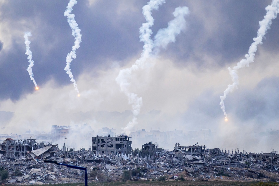 Décombres d’une zone du nord de Gaza touchée par des frappes israéliennes, le 22 novembre 2023. Dans le ciel, au-dessus des nuages de fumée, quatre traces de projectiles tirées par des fusées éclairantes sont également visibles. 