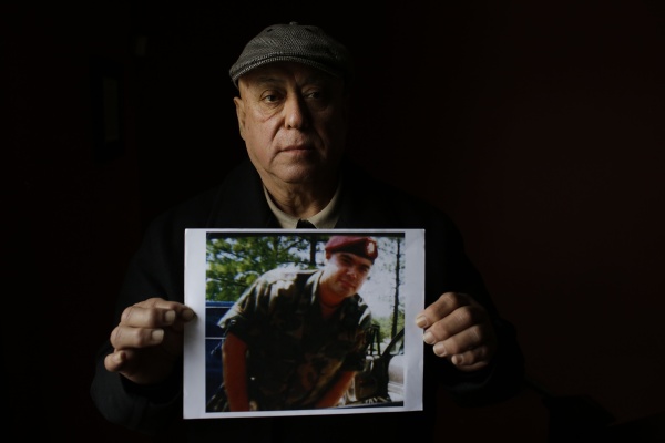 A man holds a photo of his son wearing a military uniform