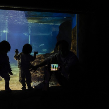 Two young children look at fish as an adult takes their photo at Sea Life Sydney Aquarium, Sydney, Australia, October 14, 2021.