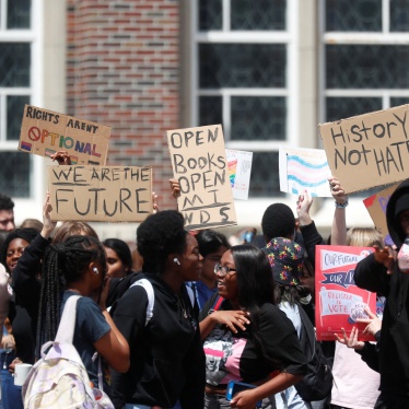 A group of high school students hold signs in front of a school building