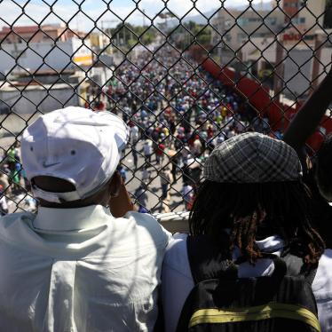 Men look at protesters marching to demand an investigation into what they say is the alleged misuse of Venezuela-sponsored PetroCaribe funds, in Port-au-Prince, Haiti, November 18, 2018. 